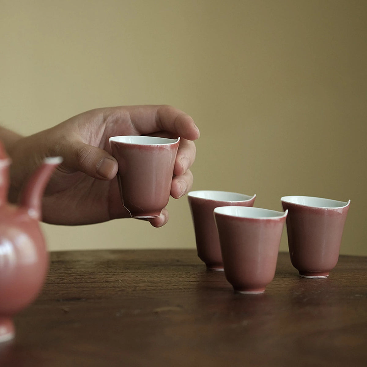 Hand holding a rose glaze tea cup with softly flared rim