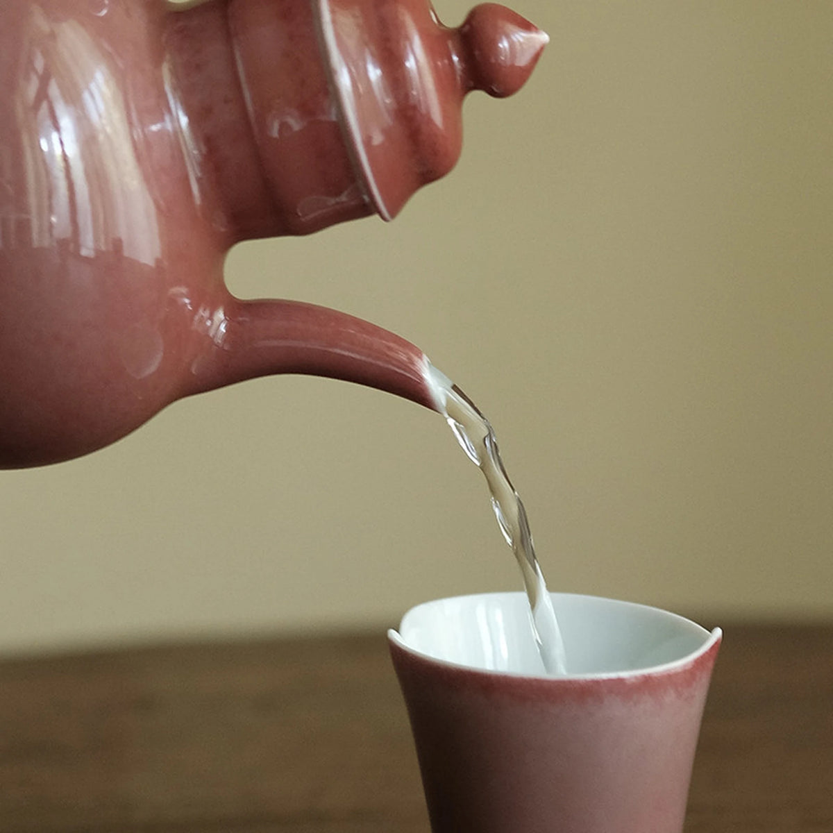 Tea pouring from the curved teapot spout into a matching cup