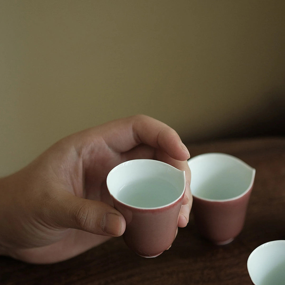 Hand holding a petite rose glaze tea cup with matching cups nearby
